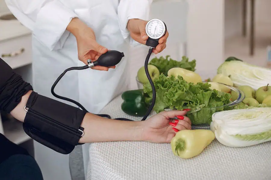 Doctor checking a patient's blood pressure next to fresh vegetables, emphasizing a healthy diet for hypertension prevention.