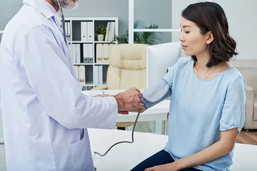 Doctor measuring a woman's blood pressure to check for hypertension in a medical office.